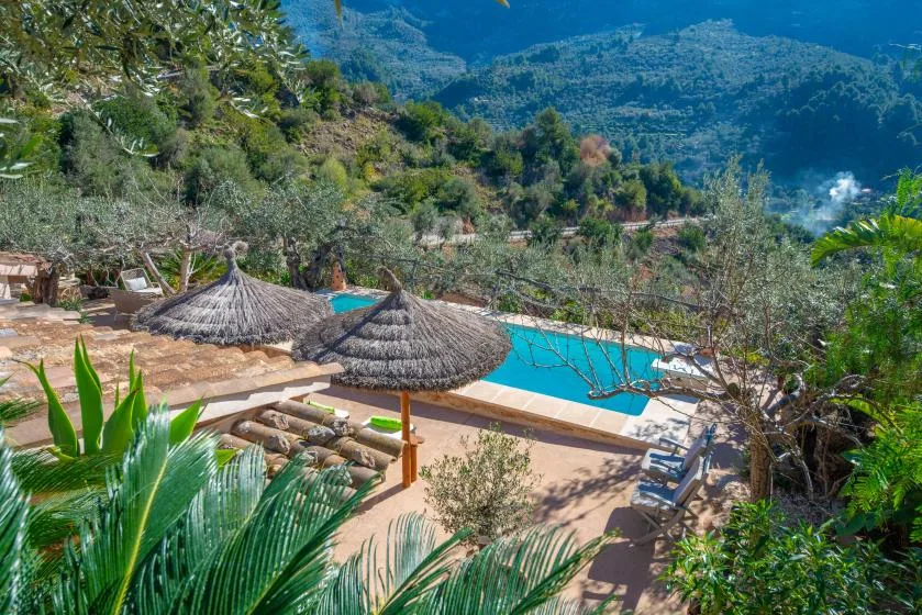 An outdoor pool and patio overlook a lush, mountainous landscape.