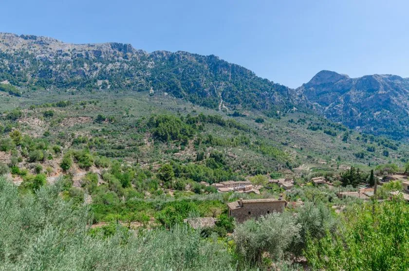 A rural landscape with green hills, scattered buildings, and mountains in the background.
