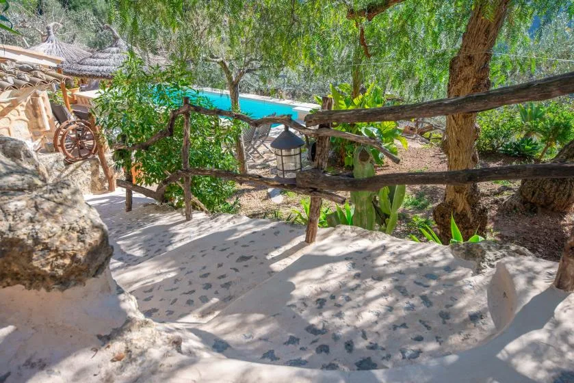 A shaded outdoor path winds through trees beside a turquoise pool.