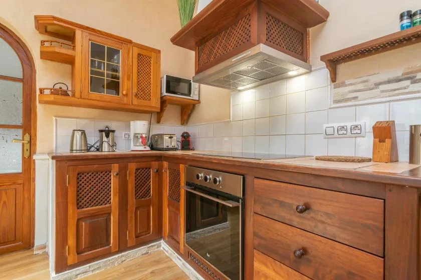 A warm-toned kitchen with wooden cabinets, a stove, and tiled walls.