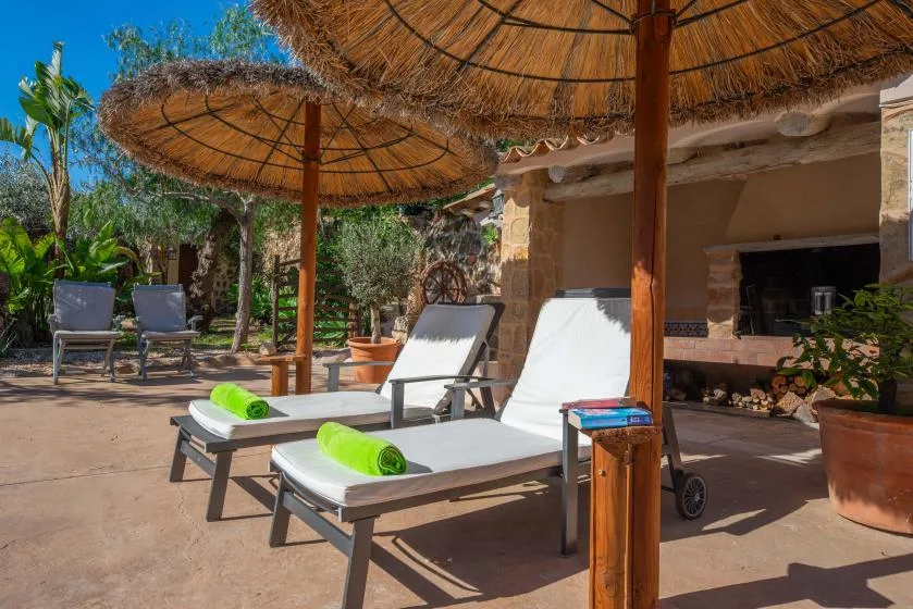 An outdoor patio has reclining seating beneath thatched parasols, beside a stone building.