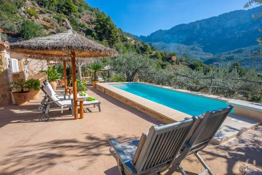 A swimming pool and lounge seating overlook a green mountain valley.