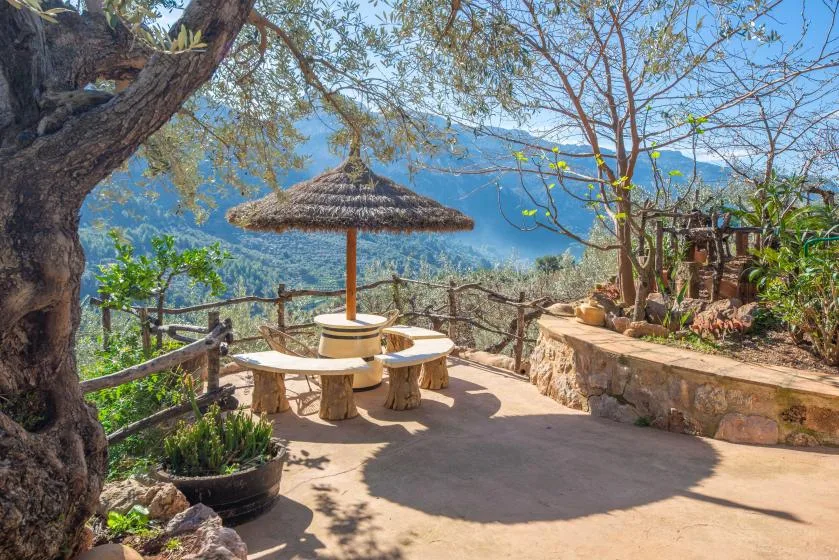 An outdoor terrace with a thatched parasol and seating overlooks a mountain landscape.