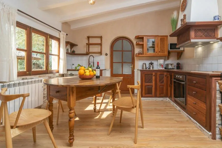 A bright kitchen with wooden cabinets, a dining table, and large windows.