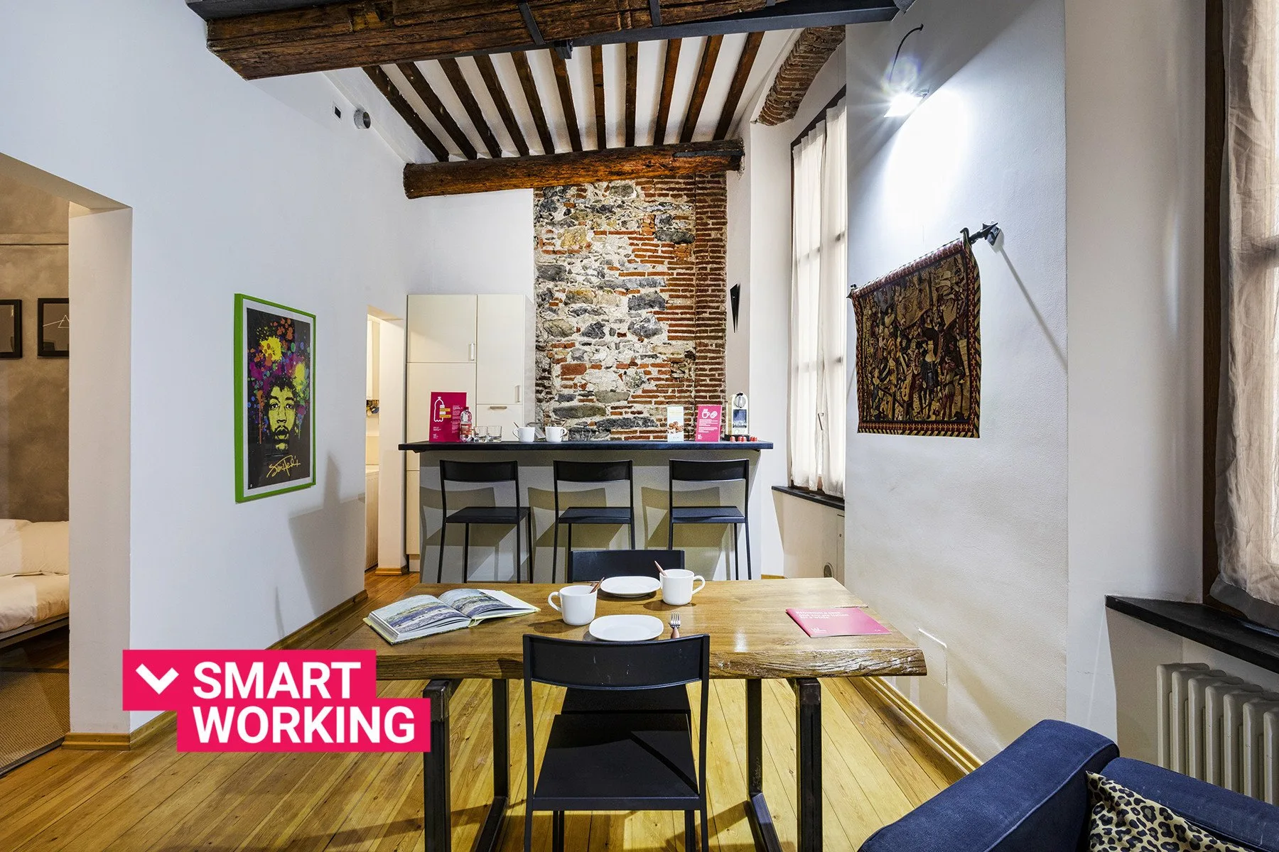 Zona de comedor y trabajo con mesa de madera, sillas y una barra bajo vigas vistas.