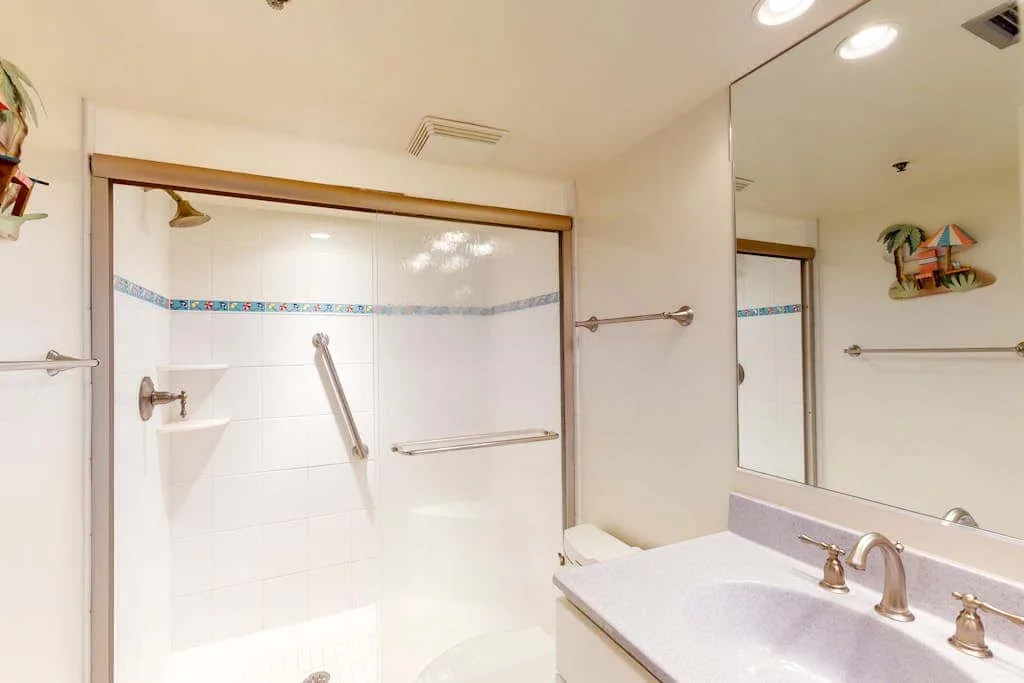 A bright bathroom with a shower and a sink beneath a large mirror.