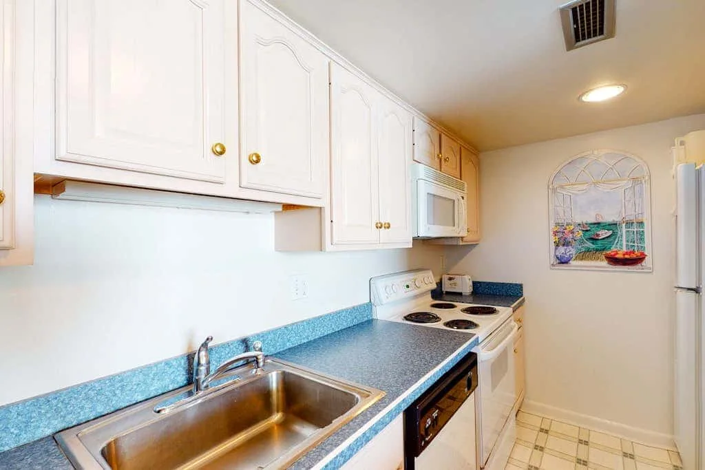 A compact kitchen with white cabinets, blue countertops, a sink, and a stove.