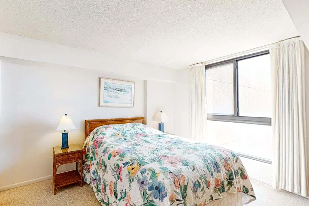 A bedroom with a floral bedspread and a large window.