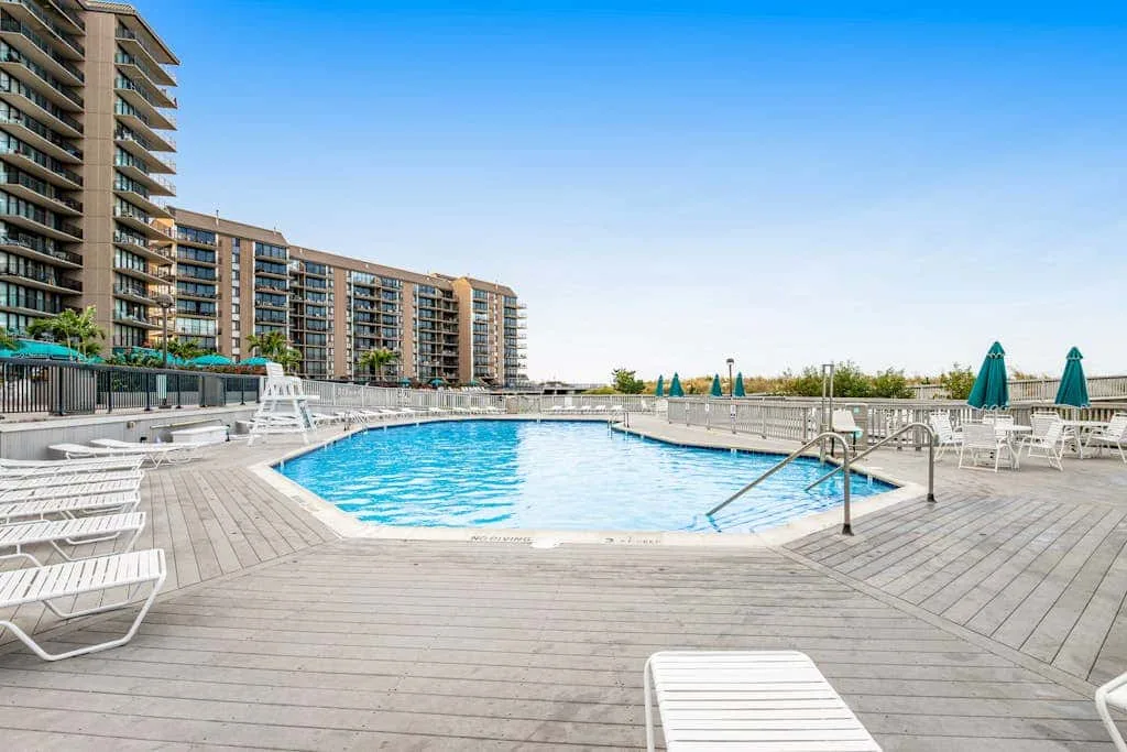 An outdoor swimming pool sits beside a wide deck with seating and umbrellas.