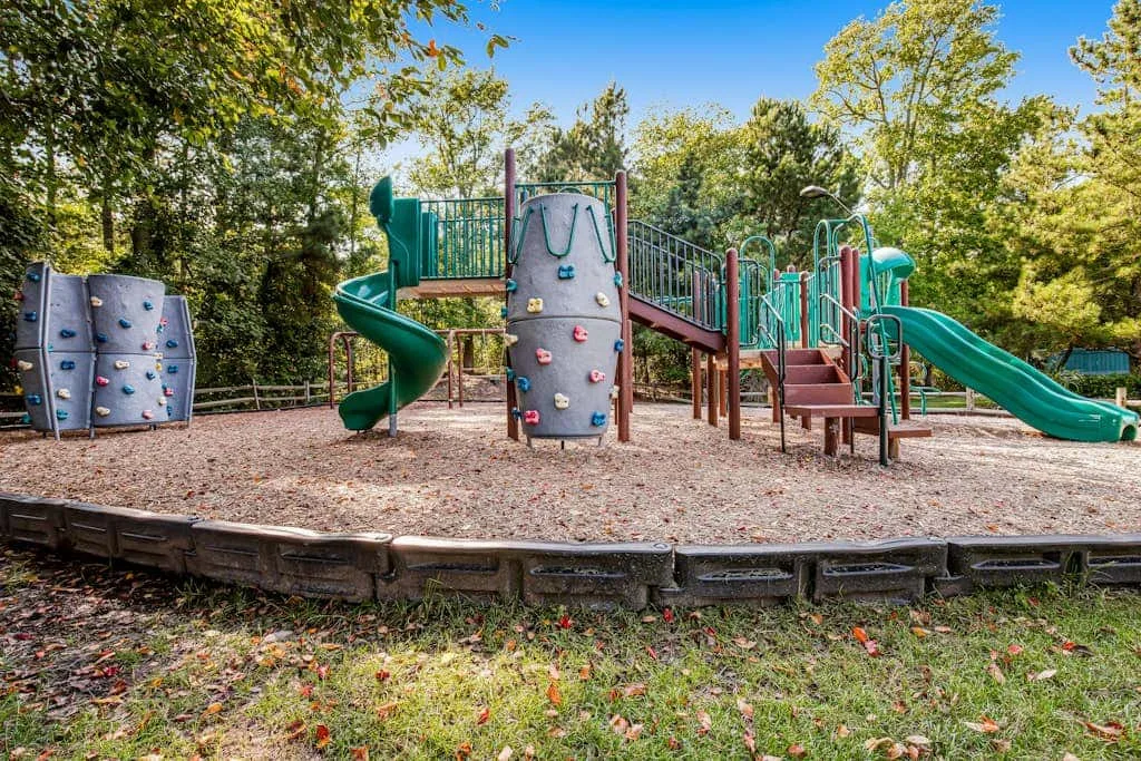 An outdoor playground features climbing walls, slides, and a wood-chip play area.