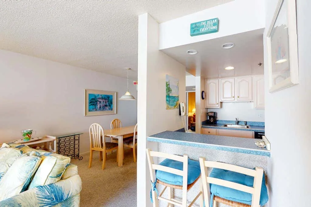 An open-plan living and dining area beside a kitchen counter with seating.