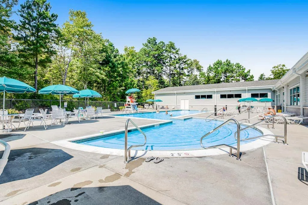 An outdoor swimming pool is surrounded by lounge seating and turquoise umbrellas.