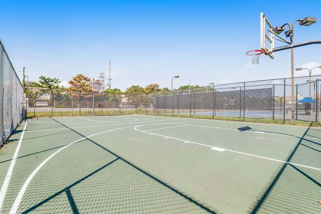 An outdoor basketball court with a hoop and surrounding chain-link fencing.