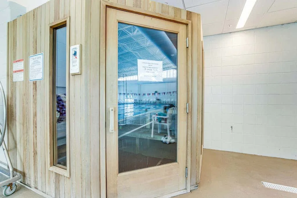 A wooden sauna room with a glass door beside a tiled wall.