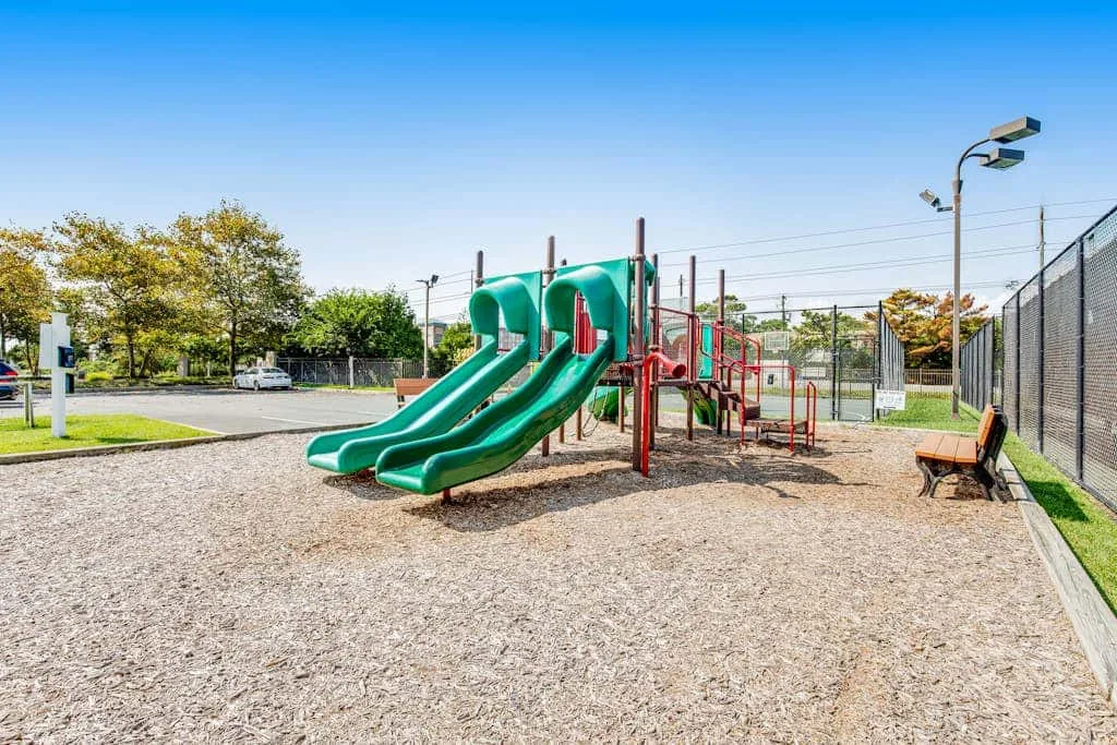 A playground with green slides and climbing equipment on a gravel surface.