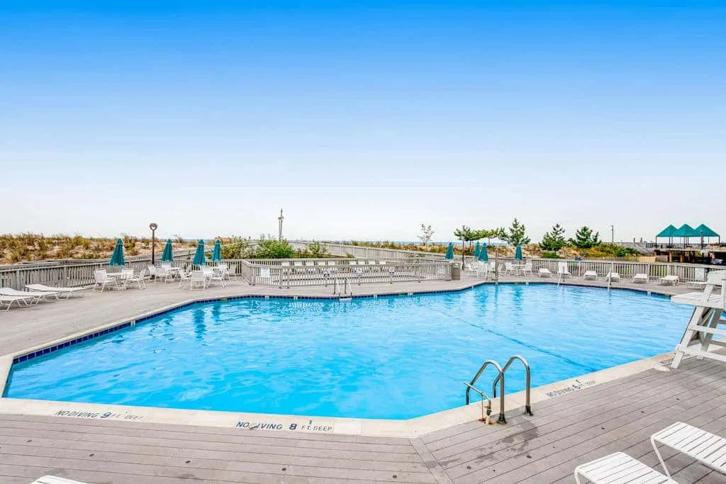A large outdoor swimming pool is surrounded by a wooden deck and lounge seating.