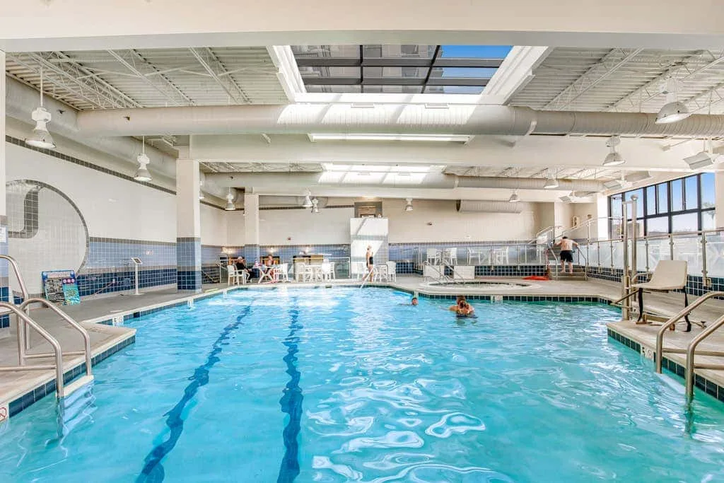 An indoor swimming pool with blue water beneath a skylit ceiling.