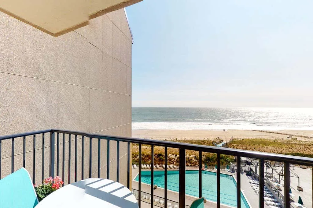A balcony overlooks a swimming pool and the beach beside the ocean.