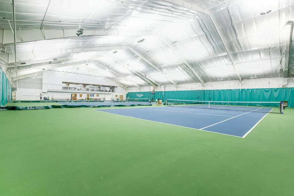 An indoor tennis court with a blue playing surface and green surrounding area.