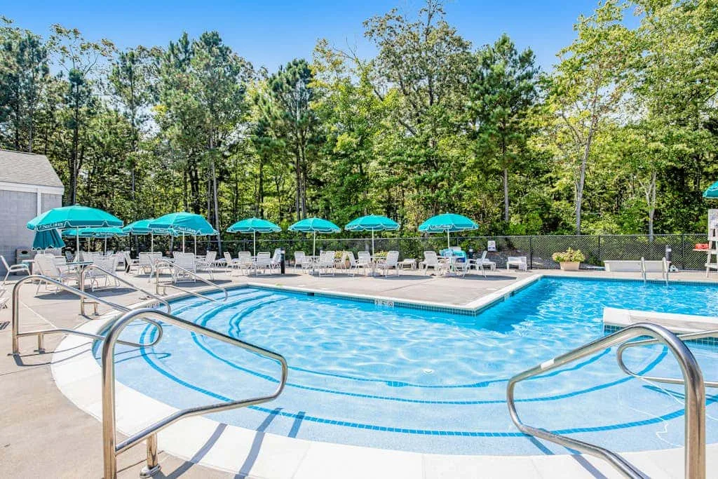 An outdoor swimming pool with turquoise umbrellas and trees around the deck.