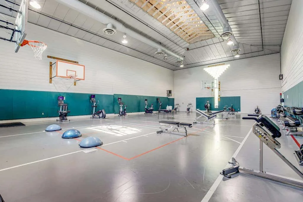 An indoor gym with exercise bikes, workout equipment, and a basketball hoop.