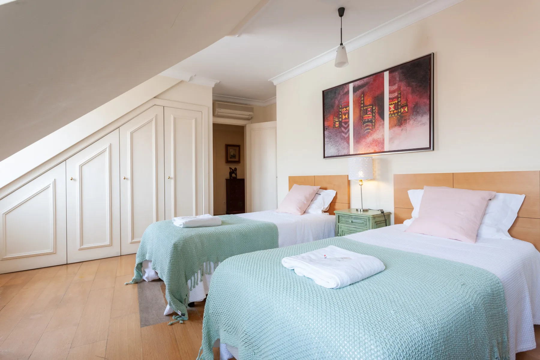 A bedroom with two beds dressed in pale green bedding.