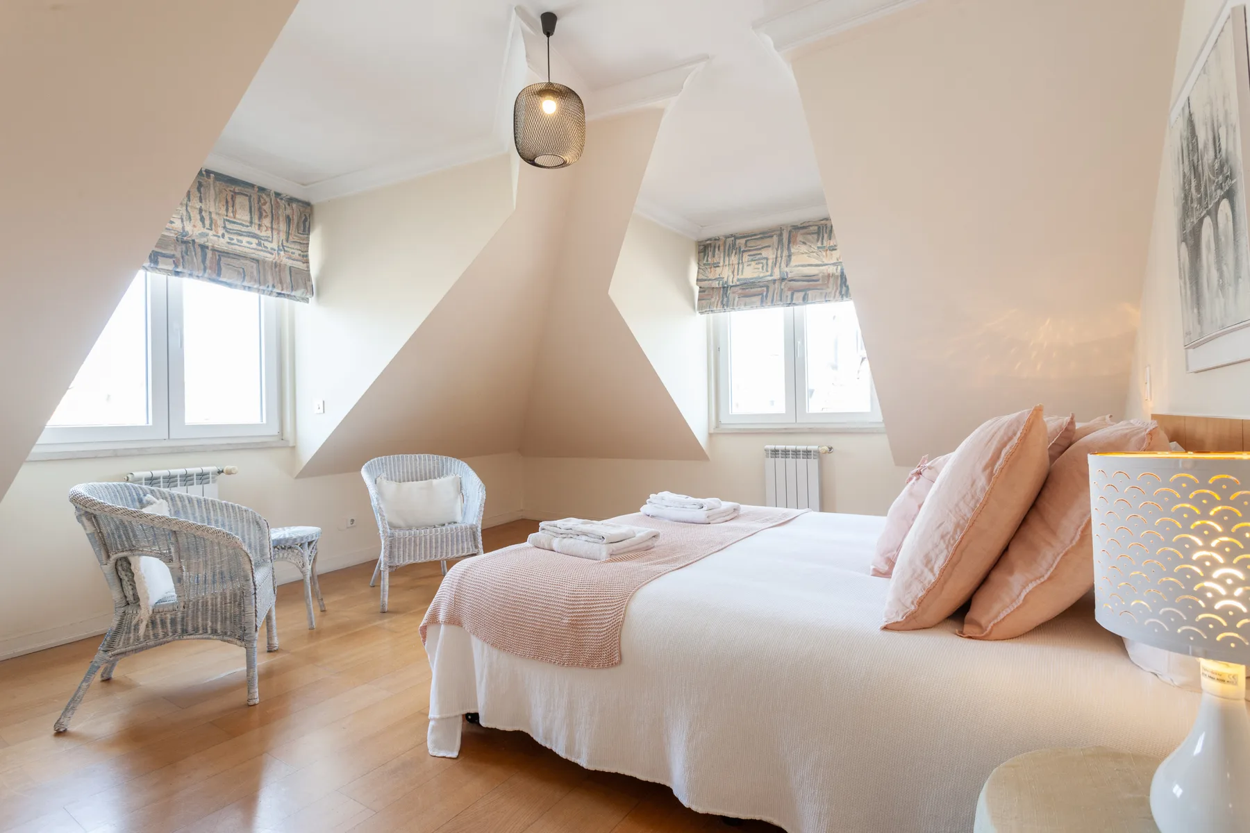 A bright bedroom with a bed, two windows, and a small seating area.