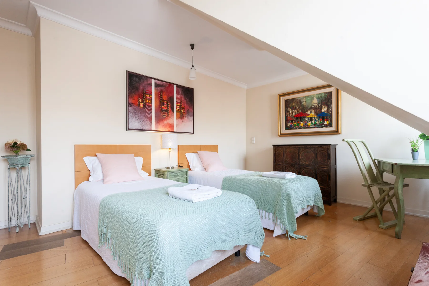 A bedroom with two beds, pale green covers, and framed artwork on the walls.