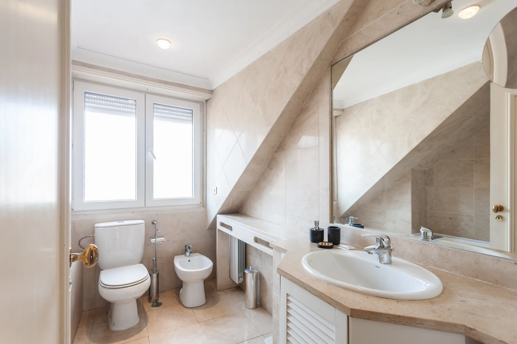 A bathroom with a toilet, bidet, and sink beneath a large mirror.