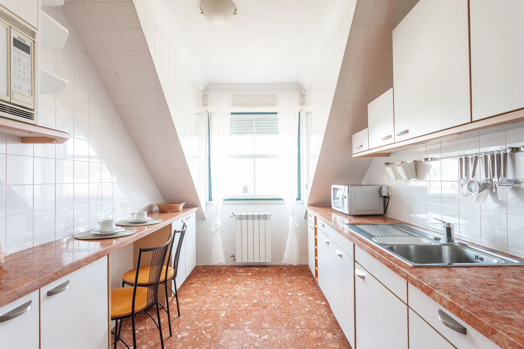 A bright galley kitchen with countertops and a window at the far end.