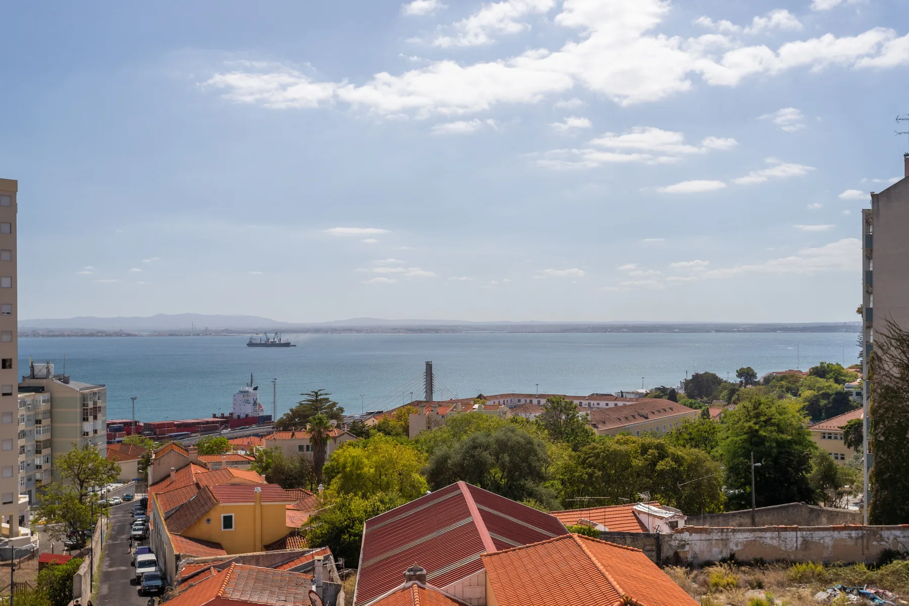 A coastal cityscape overlooks the water, with red-tiled rooftops and greenery in the foreground.