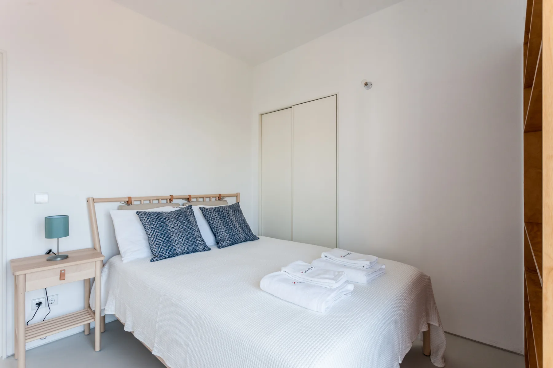 A bright bedroom with a neatly made bed and folded towels.