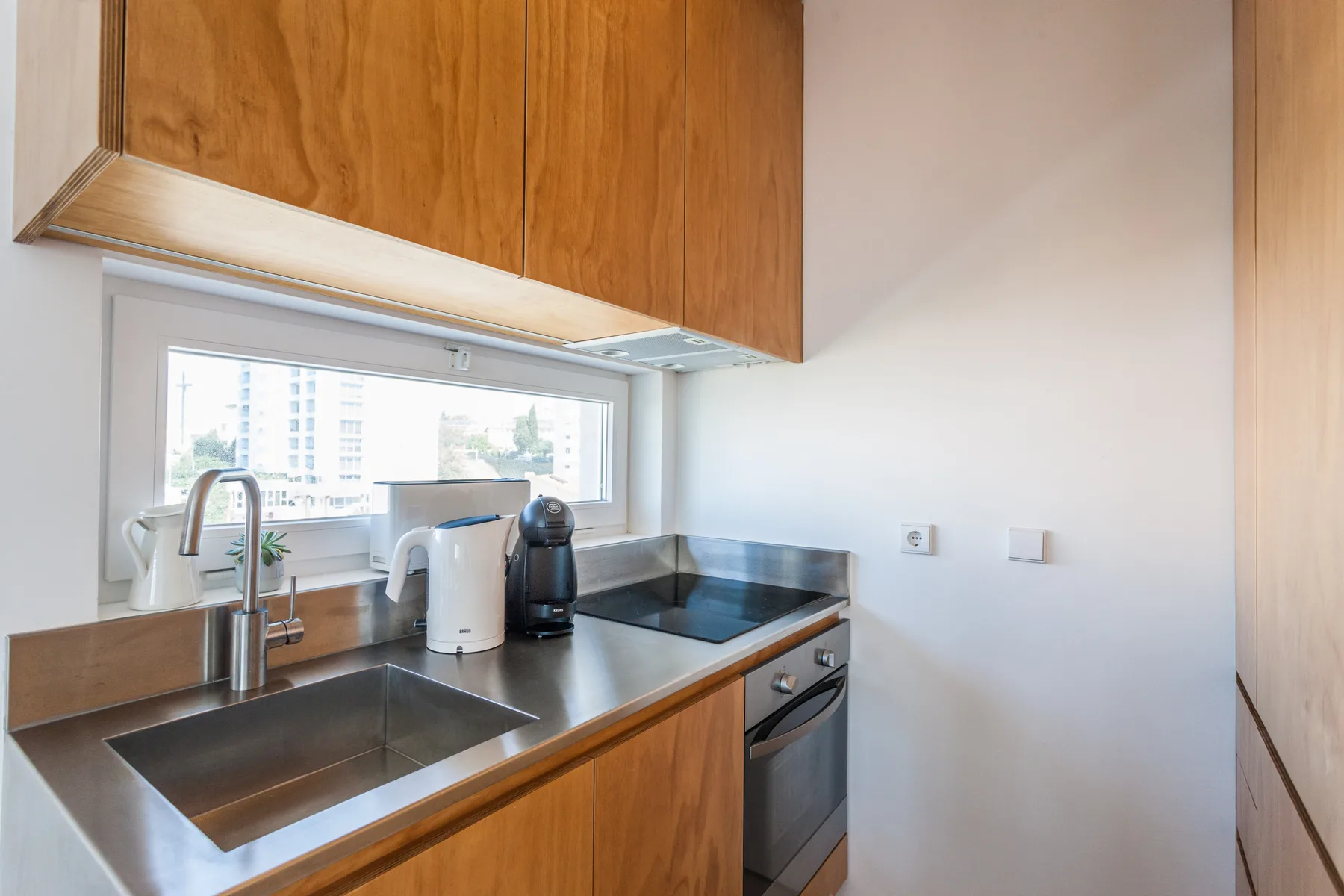 A compact kitchen with wooden cabinets, a sink, and a cooktop beneath the window.
