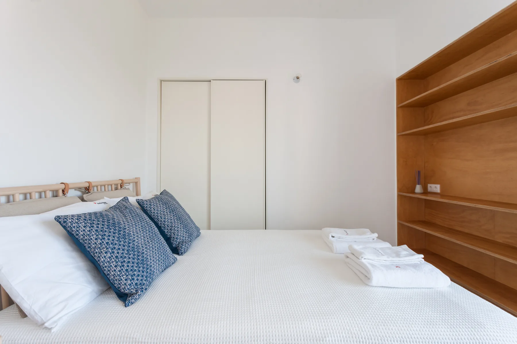 A bright bedroom with a bed and built-in wooden shelving.