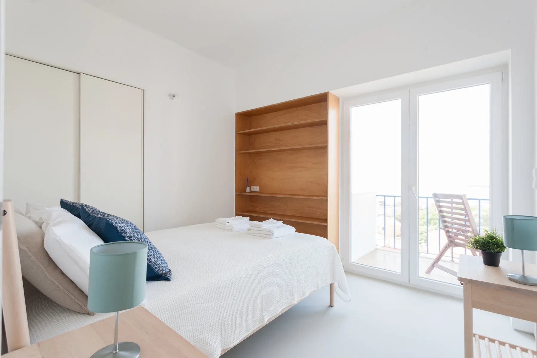 A bright bedroom with a neatly made bed beside a large glass door.
