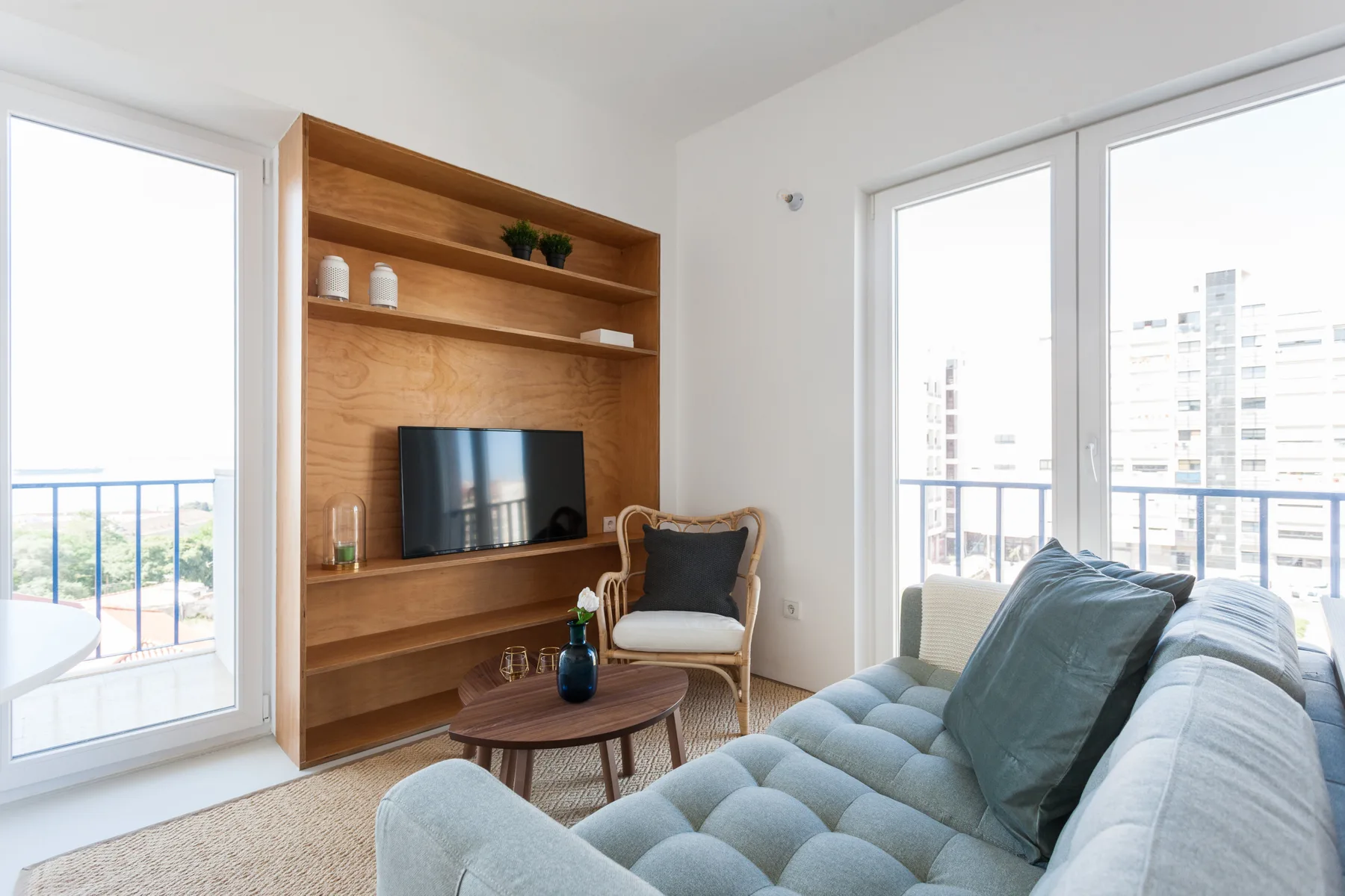 Bright living room with a television, seating, and large windows opening onto balconies.