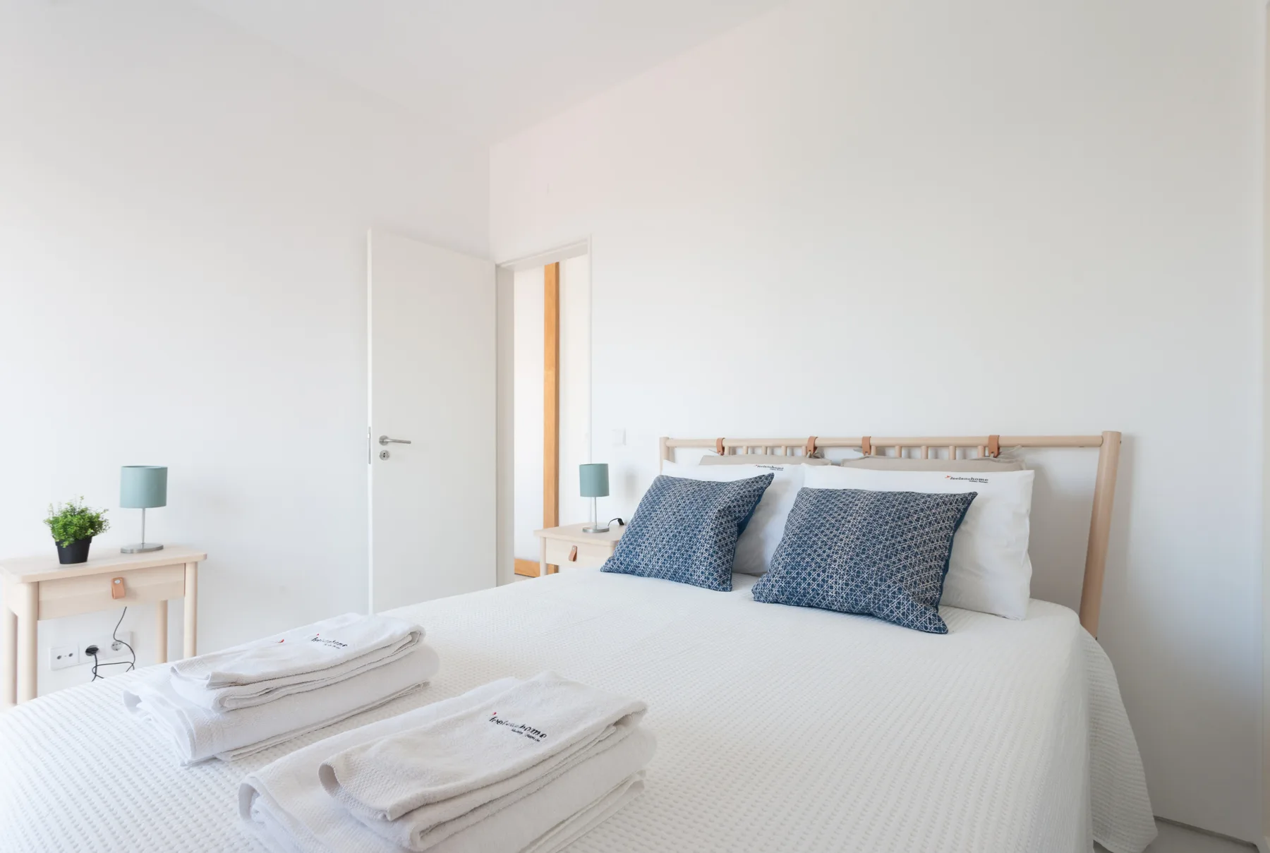 A bright bedroom with a bed, patterned pillows, and folded towels.