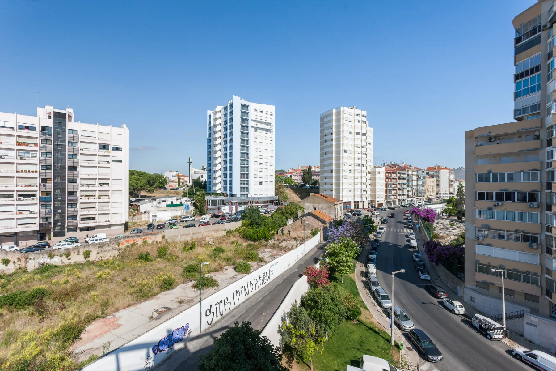 An urban neighborhood with apartment buildings, a road, and a clear blue sky.
