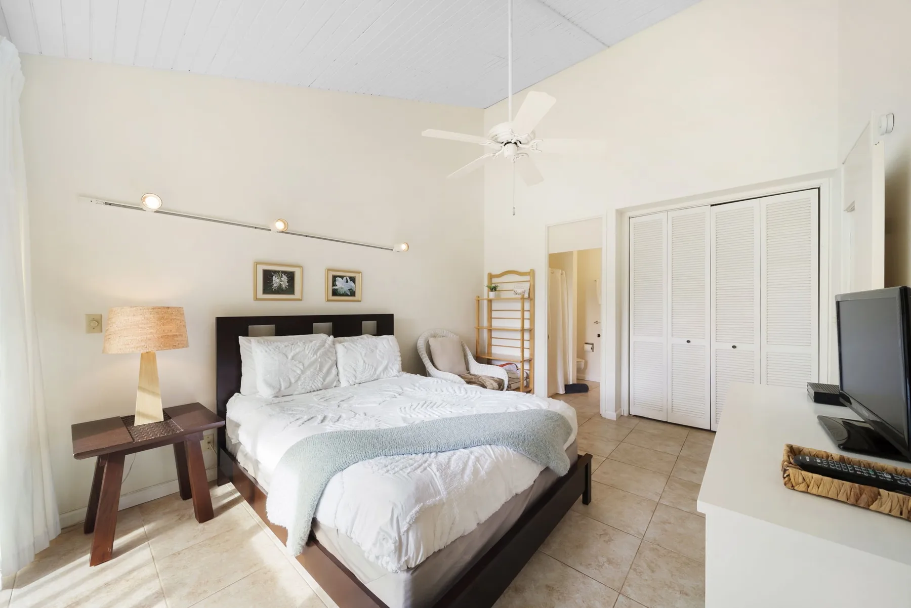A bright bedroom with a neatly made bed and ceiling fan.