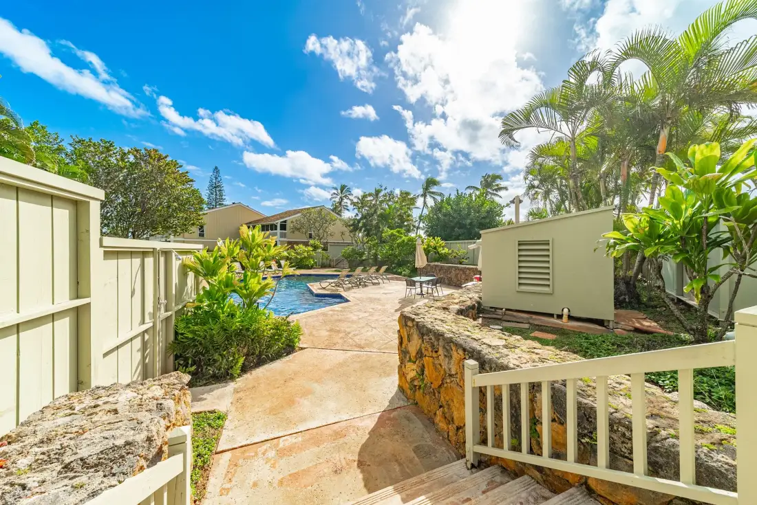 A landscaped outdoor pool area with a paved walkway and tropical plants.