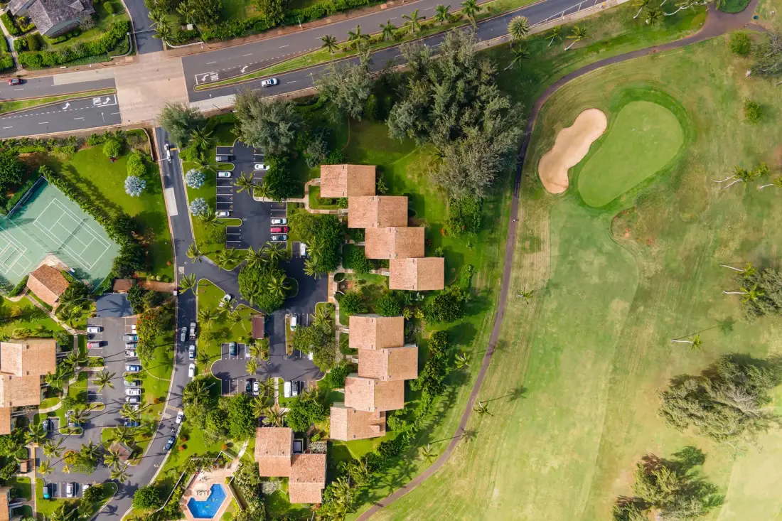An aerial view shows buildings and a parking area beside a golf course.