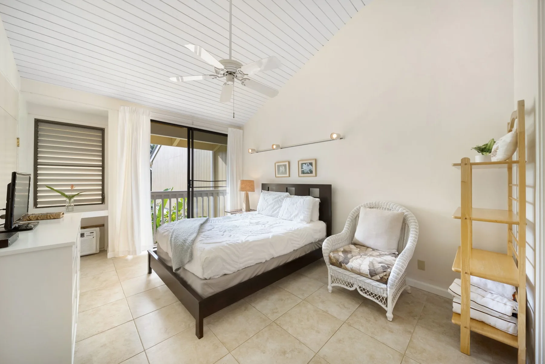 A bright bedroom with a bed, a wicker chair, and sliding glass doors.