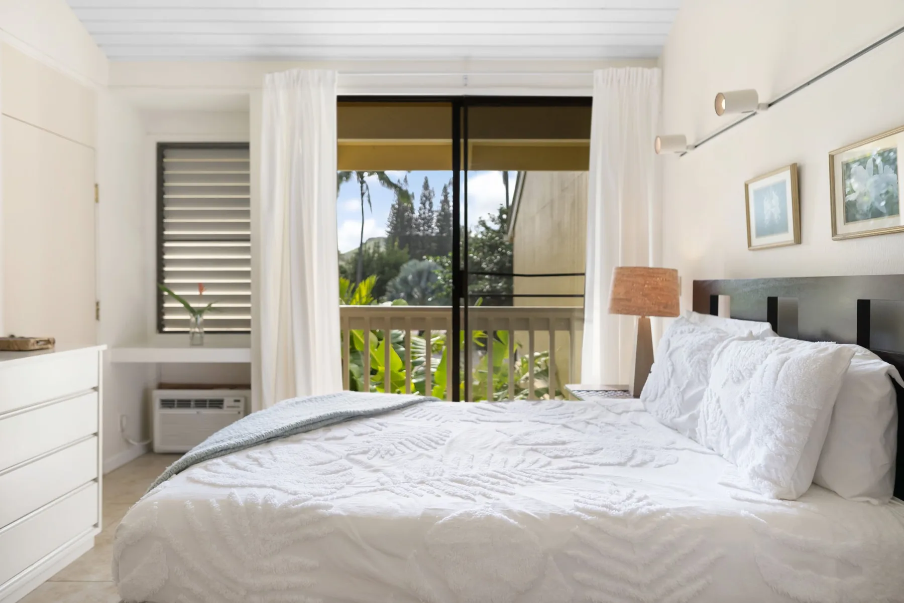 A bright bedroom with a white bed and glass doors opening onto a balcony.