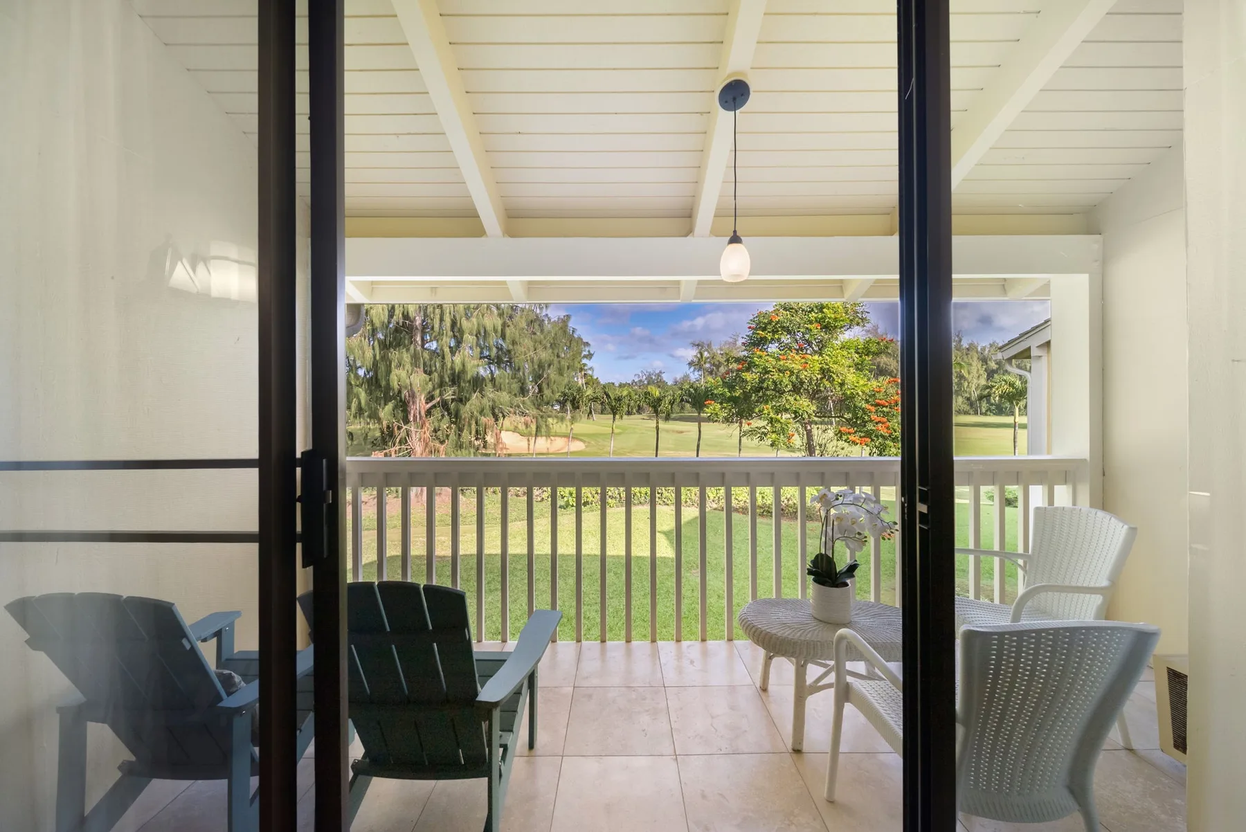A covered patio with outdoor seating overlooks a green lawn and trees.