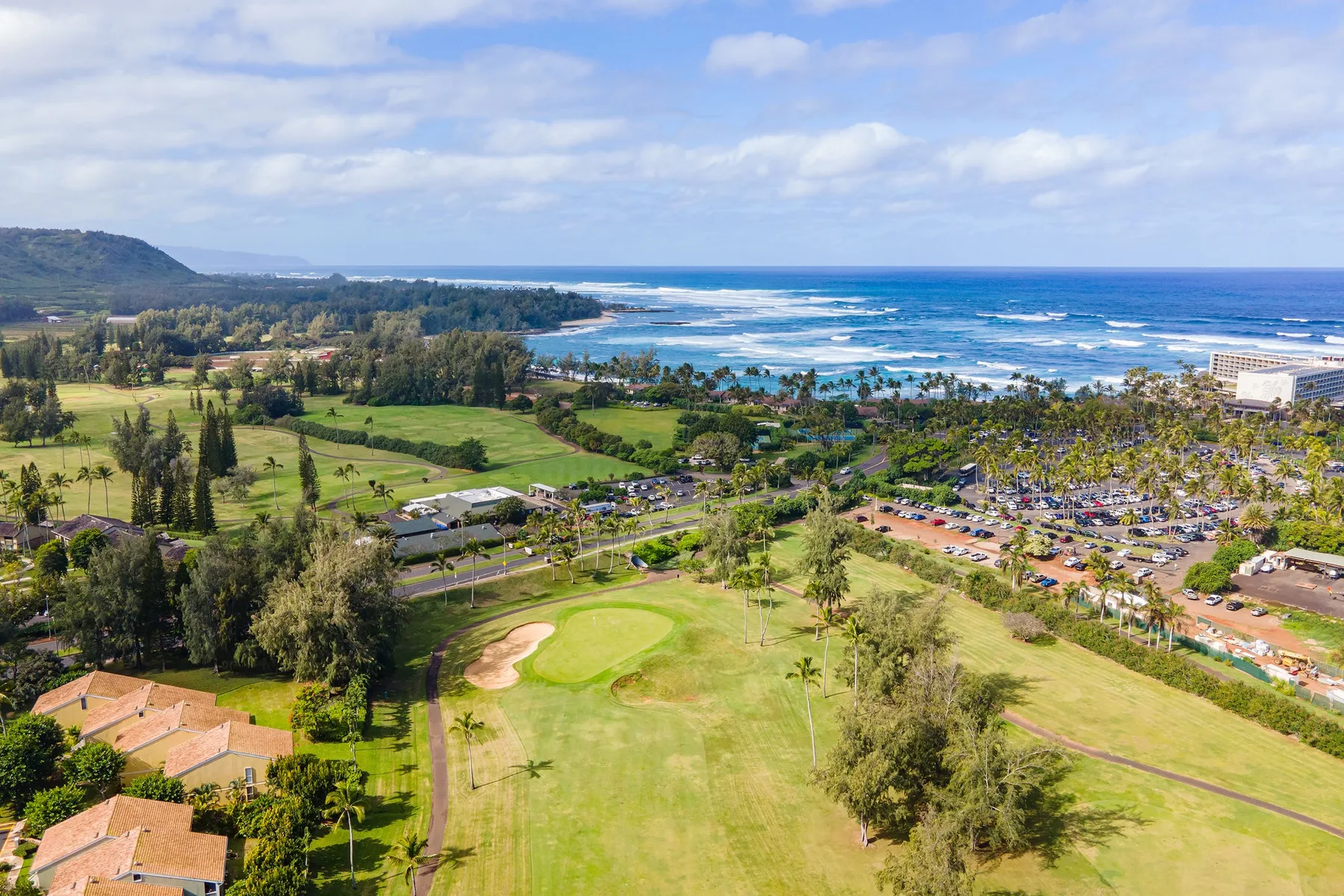 A coastal golf course overlooks green fairways, trees, and the ocean.