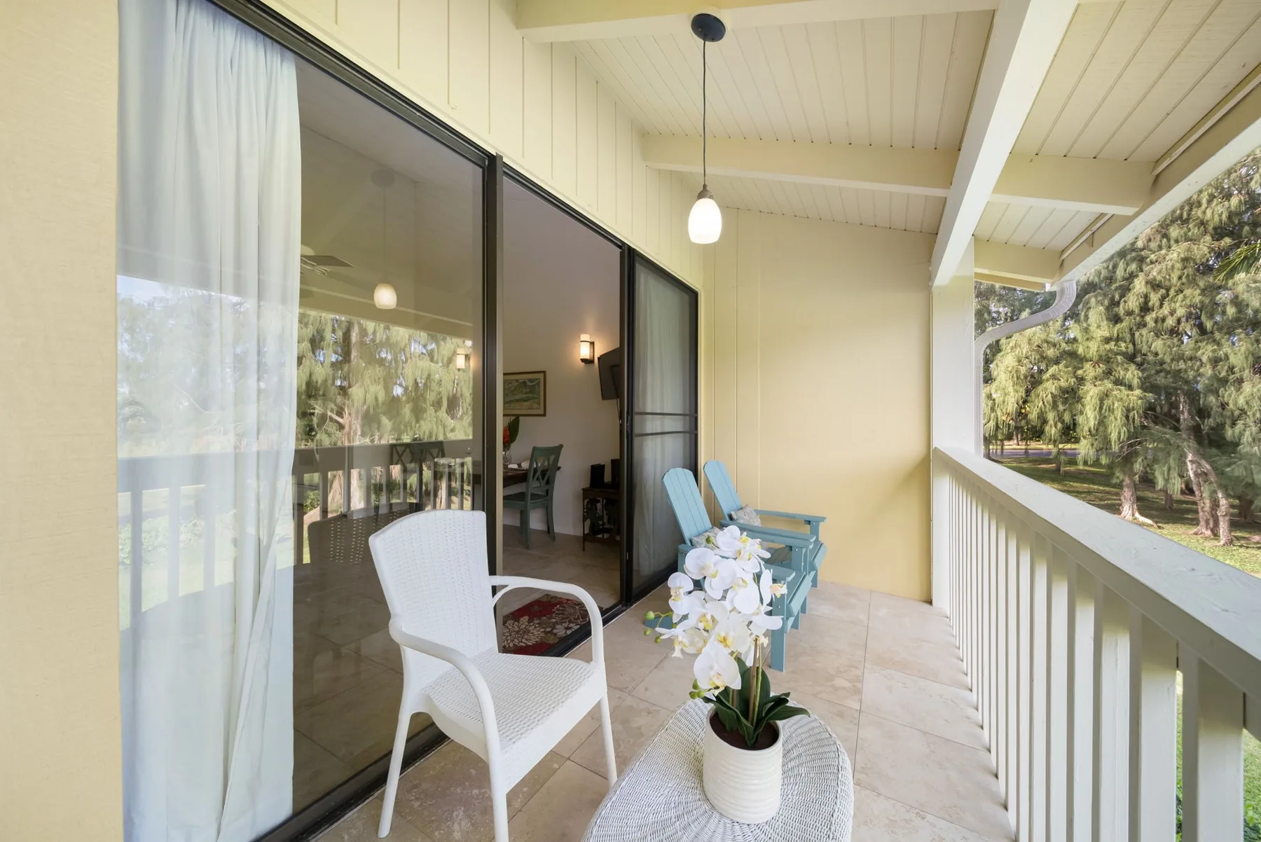A covered balcony has seating beside sliding glass doors and a view of trees.