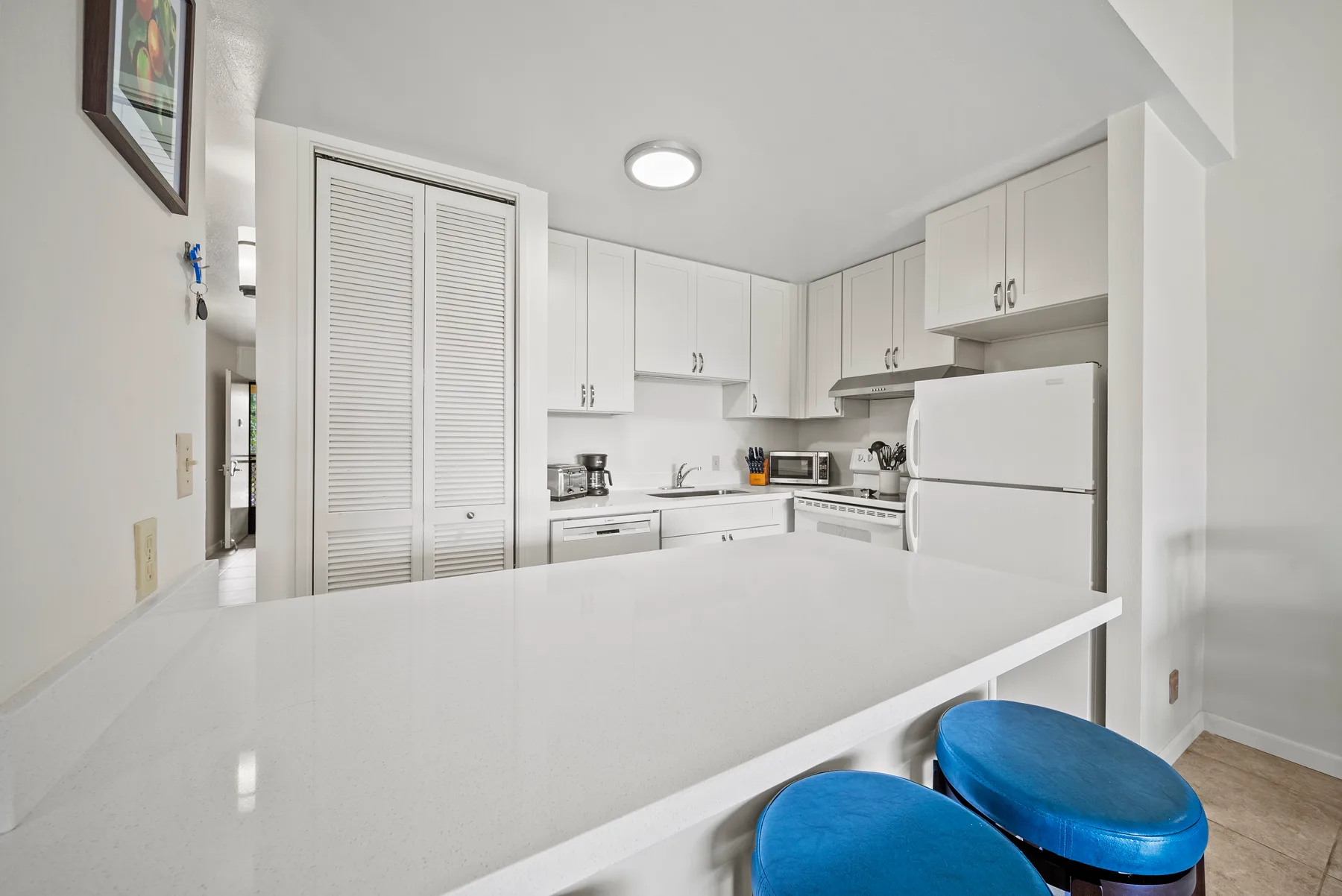 A bright white kitchen with a wide counter and blue seating.