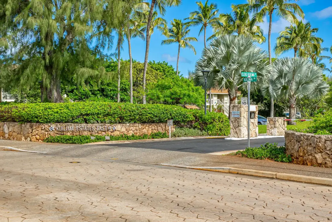 A landscaped community entrance with stone walls and palm trees.
