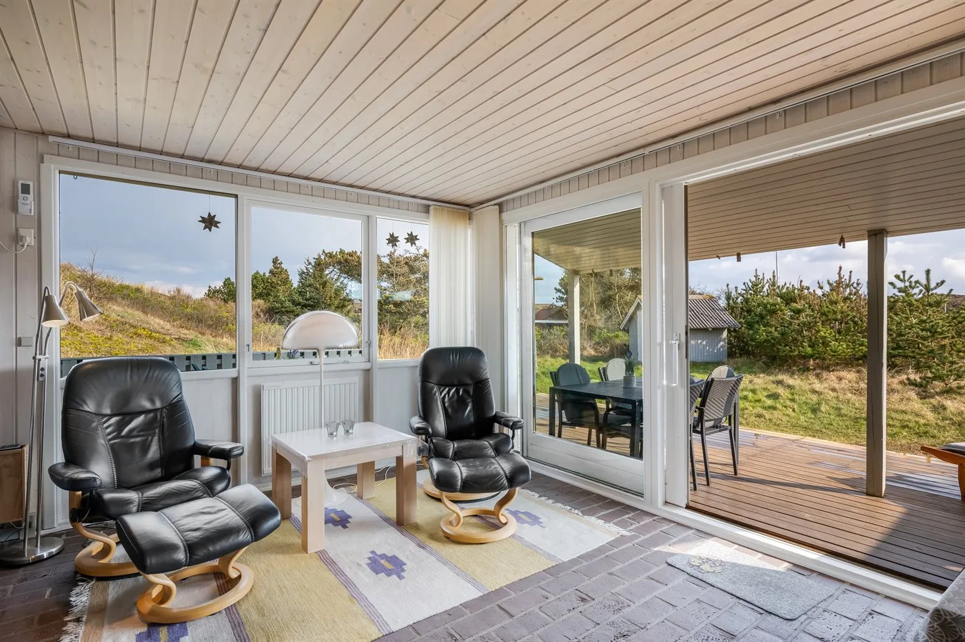 Una sala luminosa con asientos reclinables junto a grandes ventanas y un patio.