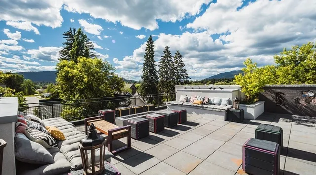 An outdoor rooftop terrace with lounge seating and a dining table overlooks a tree-lined landscape.